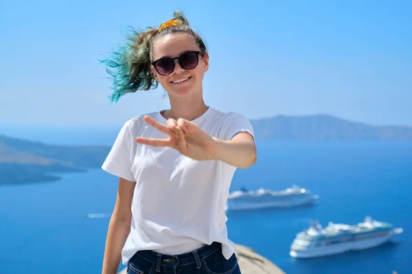 Young beautiful teenager girl tourist posing smiling, background summer sunny scenic sea landscape with white cruise liners in Aegean Sea on famous Greek island Santorini