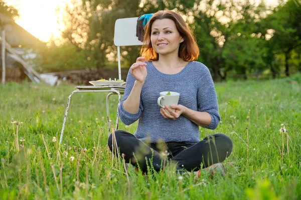 美丽而成熟的女园丁坐在草地上 喝着天然草茶 乡村风情 夕阳西下 金碧辉煌 — 图库照片