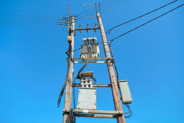 Electric transformer on wooden poles, blue sky background.