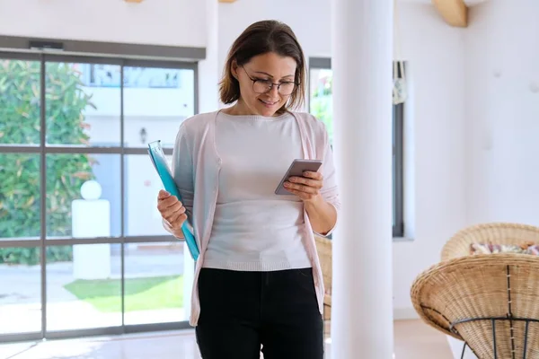 Business woman with smartphone and clipboard in hotel interior.