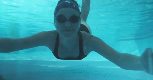 Atlético adolescente chica nadador bajo el agua en azul piscina al aire libre, mirando a la cámara — Vídeos de Stock