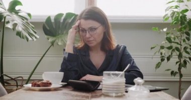 Elinde çay fincanı olan pijamalı olgun bir kadın dijital tablet okuyor, kötü haber.