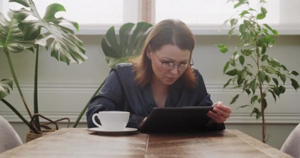 Desayuno mujer madura en pijama con taza de té lectura tableta digital, malas noticias — Vídeos de Stock