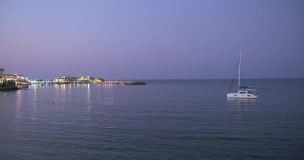 Yunanistan, Girit, 09-09-2019. Deniz akşam manzarası. Deniz koyunda küçük bir yat, iskele ve deniz feneri ışıkları. — Stok video