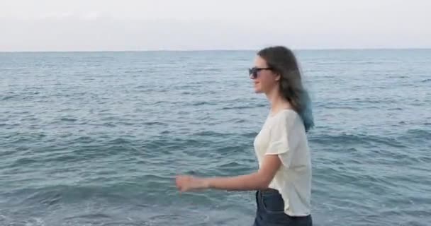 Zee avond landschap, trendy mooie glimlachende tiener meisje wandelen langs het strand — Stockvideo