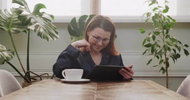 成熟した女性はデジタルタブレットでテーブルで朝食を持っている良いニュースを読む — ストック動画