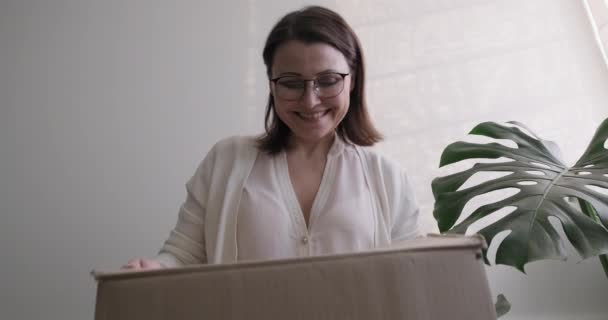 Зрелая женщина распаковывает картонную коробку на столе дома, в офисе — стоковое видео