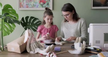 Anne ve kızı birlikte oyuncak tavşan bebeği dikiyorlar, hobileri ve evde boş vakitleri var.
