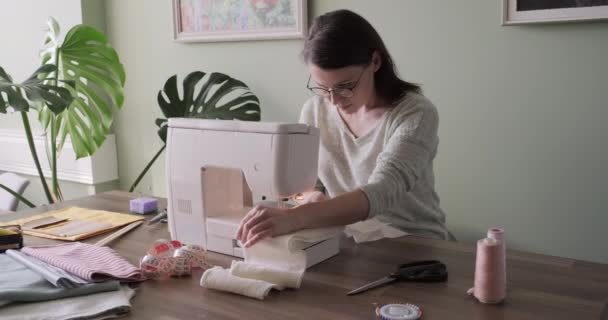 Mujer adulta cose en una máquina de coser sentada en casa en la mesa — Vídeos de Stock