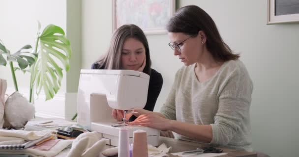 Мама учит дочь шить на машинке, женщины шьют игрушки и одежду для игрушек — стоковое видео