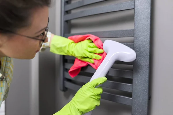 Woman cleaning heated towel rail, using steam machine