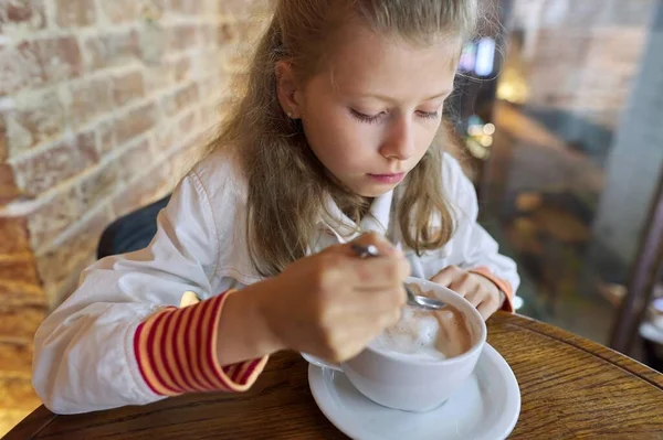Niña de 9 años, 10 años con taza de chocolate caliente sentado en la cafetería en la mesa — Foto de Stock