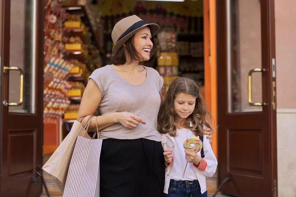 Улыбающиеся мать и дочь ребенка, идущие от магазина карамельных конфет — стоковое фото