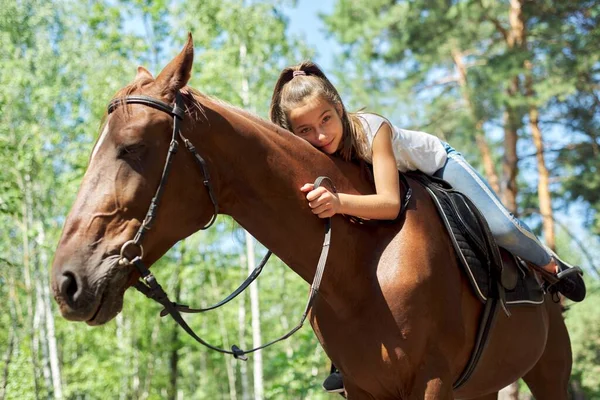 Menina criança equitação cavalo, verão cavalo passeio na floresta, menina amorosamente abraçado cavalo — Fotografia de Stock