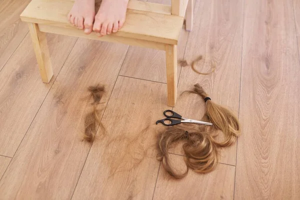 Cabello recortado de niña y tijeras en el suelo en casa —  Fotos de Stock
