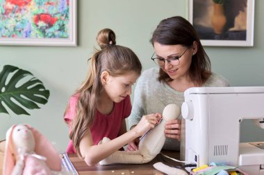 Mutlu anne ve kız evde oyuncak bebek dikiyorlar.