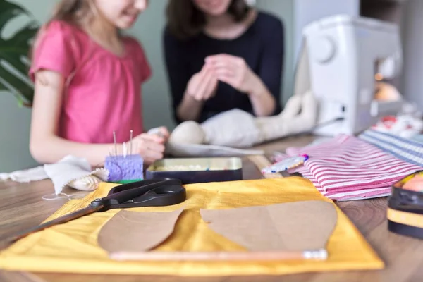 Niños sentados en casa, cosiendo muñecas, en desenfoque, fondo. Primer plano de la tela, patrones, plantillas, tijeras, hilos, agujas — Foto de Stock