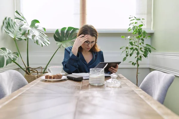 Sério mulher madura trabalhando em casa, usando tablet digital, caderno de negócios — Fotografia de Stock