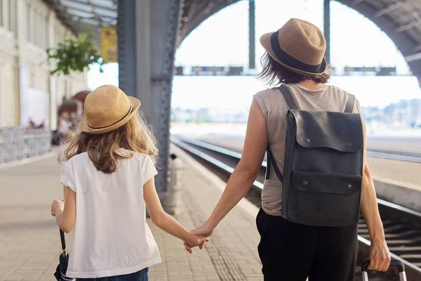 Madre feliz e hija niño caminando juntos en la estación de tren con maleta, vista trasera — Foto de Stock