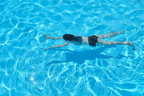 Mujer joven en bikini nadando bajo el agua en una piscina al aire libre, vista superior — Foto de Stock