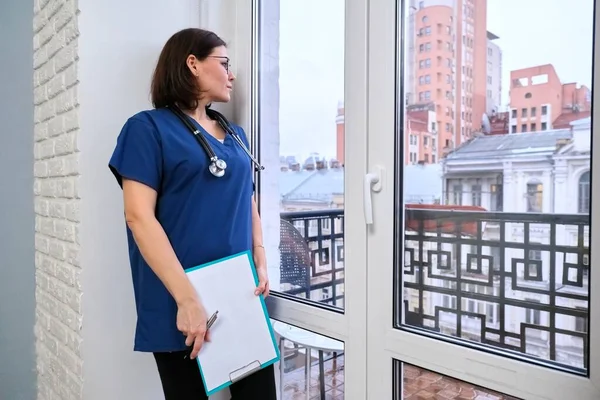 Enfermeira com ficha médica no escritório a olhar pela janela — Fotografia de Stock