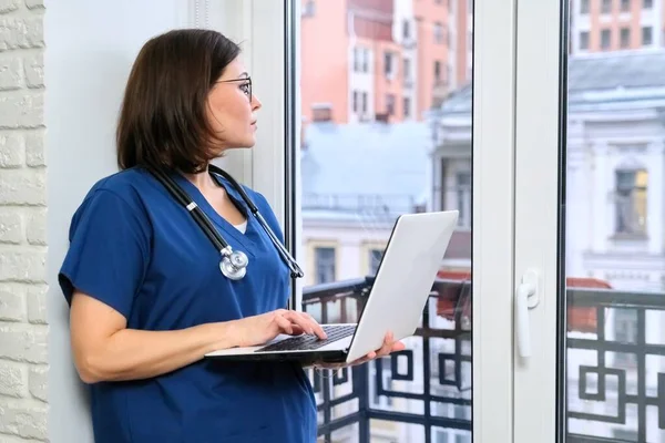 Enfermeira feminina usando computador portátil, médico perto da janela no consultório da clínica — Fotografia de Stock
