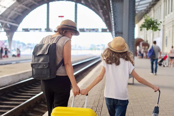 Madre feliz e hija niño caminando juntos en la estación de tren con maleta, vista trasera —  Fotos de Stock