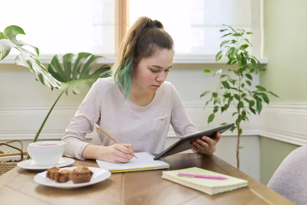 Teenager dívka studuje doma, student sedí u stolu pomocí digitálního tabletu — Stock fotografie