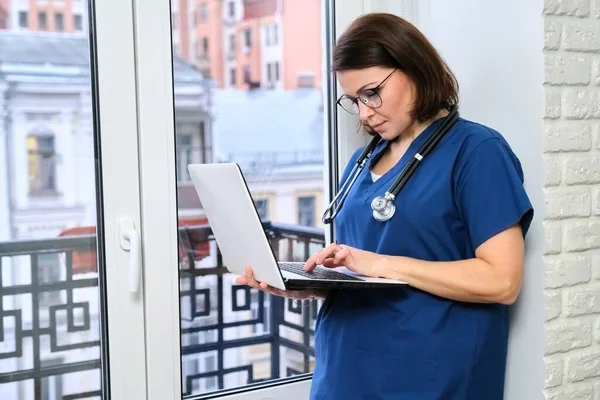女护士用手提电脑，医生在诊所窗口附近 — 图库照片