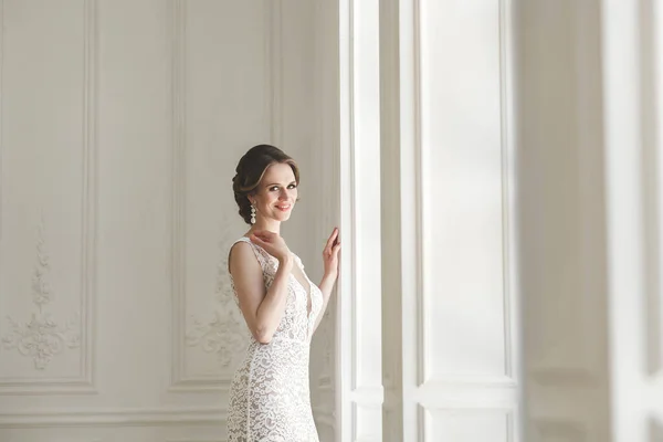 白の写真スタジオのウェディング ドレスでポーズ美しい花嫁。ミラー。ソファ。花束。その戸。シャンデリア. — ストック写真
