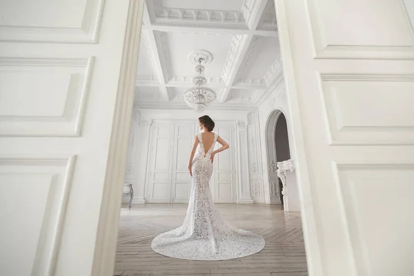 美丽的新娘摆在婚纱礼服在一个白色的摄影棚。镜子.沙发.束.门。吊灯. — 图库照片