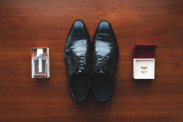 Scarpe nere, anelli di fidanzamento e profumo da uomo sul pavimento. Accessori per lo sposo il giorno del matrimonio . — Foto Stock