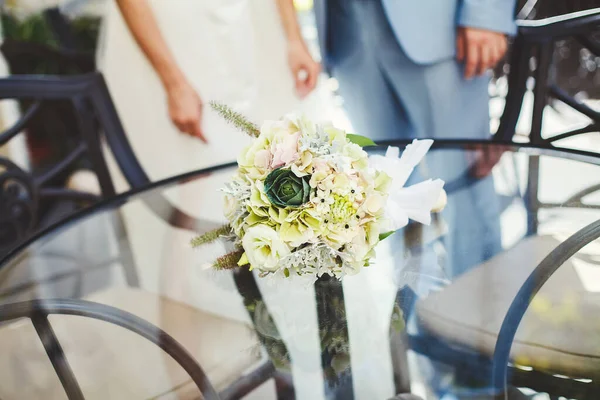 Bukiet ślubny białych i zielonych kwiatów leży na szklanym stole. — Zdjęcie stockowe