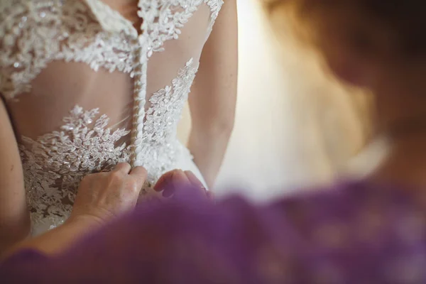 Družička dělá luk-uzel na zadní straně nevěsty svatební šaty. — Stock fotografie