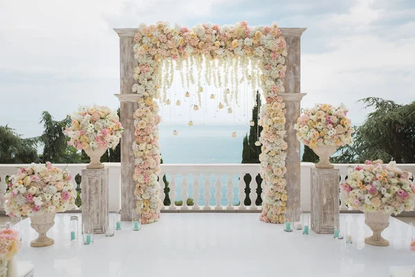 Elegant bröllop båge med färska blommor, vaser på bakgrunden av havet och blå himmel. — Stockfoto