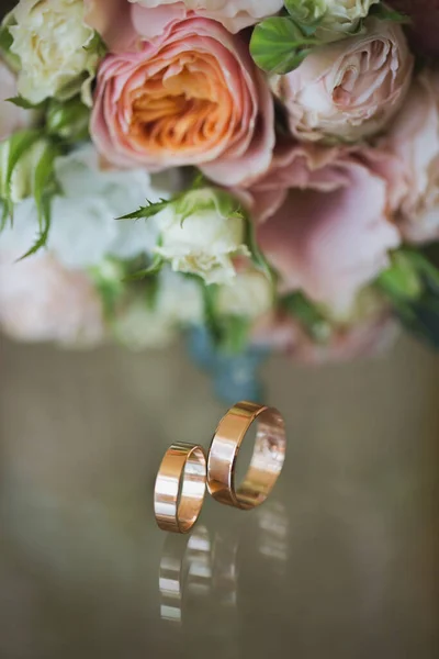 Gold wedding rings with a bouquet on the table. — Stock Photo, Image