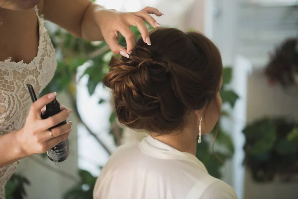 Master stylist maakt de bruid huwelijkskapsel met vaststelling van de lak spray. — Stockfoto