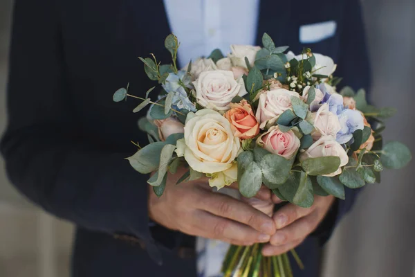 Elegante novio sosteniendo un tierno ramo de boda rosa . — Foto de Stock