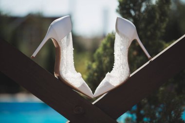 Havuzun arka planındaki ahşap kirişin üzerinde zarif beyaz düğün ayakkabıları..