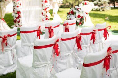 Düğün töreni açık havada. Kırmızı kurdeleli beyaz sandalyeler.