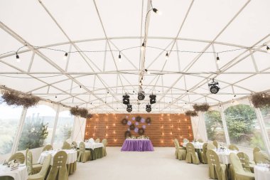 Beyaz bir çadırda düğün resepsiyonu. Mor çiçek dekoru.