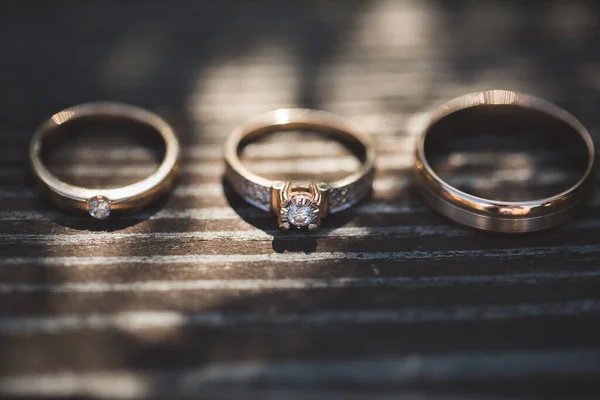 Tres anillos sobre fondo de madera. Anillo de compromiso y dos bandas de boda en la mesa de madera. Joyería de boda de oro blanco . — Foto de Stock