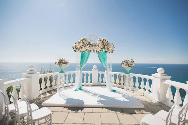 Elegant bröllop båge med färska blommor, vaser på bakgrunden av havet och blå himmel. — Stockfoto