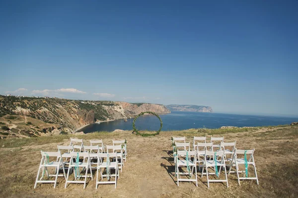 Bröllopsvalv i form av en ring och vita stolar på en klippa mot bakgrunden av havet. — Stockfoto