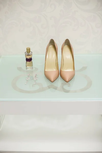 Свадебная обувь кремового цвета, белая на стеклянном столе. Духи. Серьги . — стоковое фото