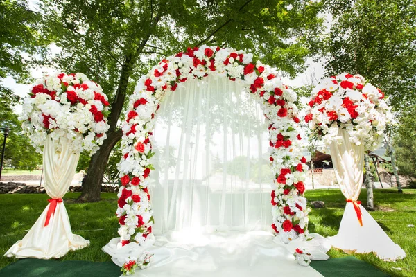 Cerimonia di matrimonio all'aperto. Arco da sposa decorato con fiori rossi . — Foto Stock