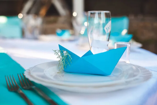 Il tavolo del ristorante per un matrimonio in stile marinaro. Carta ospiti in una barca di carta blu. — Foto Stock