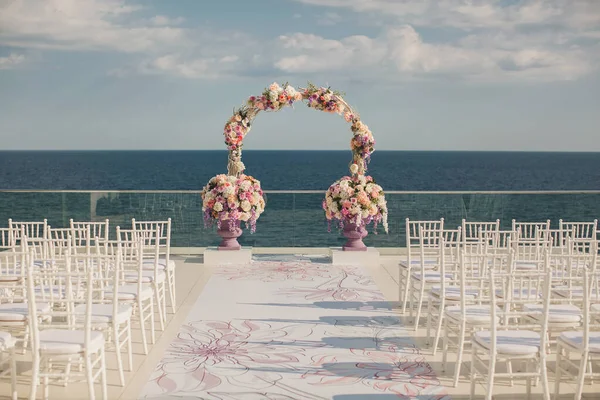 Bröllopsbåge med färska blommor på en havsbakgrund. Vaser med färska blommor. — Stockfoto