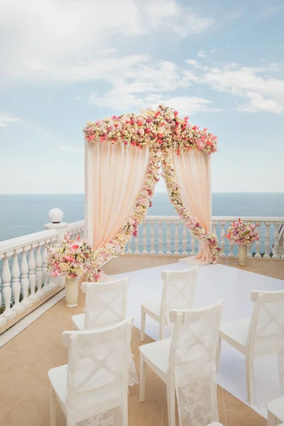 Bruiloft boog perzik kleur met bloemen op de achtergrond van de zee. Vazen met verse bloemen. — Stockfoto