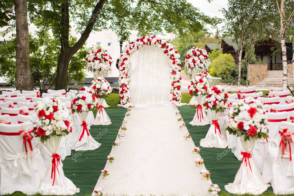 Wedding ceremony outdoors. Wedding arch decorated with red flowers.